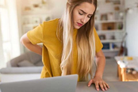 Tired woman suffering backache while using laptop