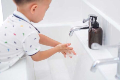 Cute little Asian 2 - 3 years old toddler boy child washing hands by himself on sink and water drop from faucet in public toilet / bathroom for kids, Clean school washrooms - soft & selective focus