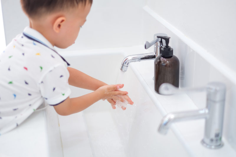 Cute little Asian 2 - 3 years old toddler boy child washing hands by himself on sink and water drop from faucet in public toilet / bathroom for kids, Clean school washrooms - soft & selective focus