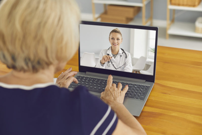 Senior woman sitting at laptop and talking to virtual doctor of e-health service