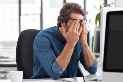 a man in office rubbing his eyes