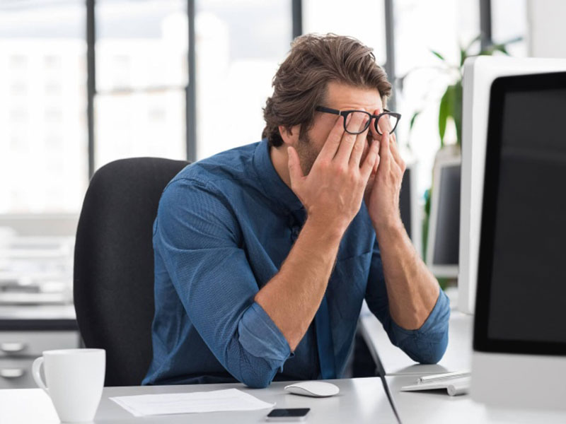 a man in office rubbing his eyes