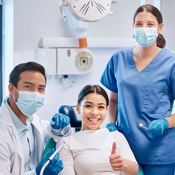 Shot of a young male dentist giving the thumbs up with his patient and assistant
