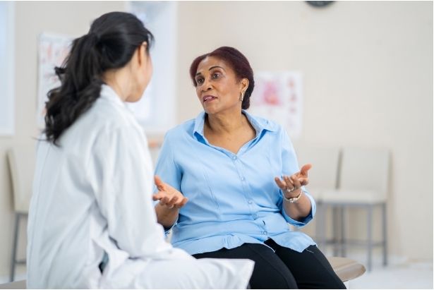 A woman sitting in an exam room talking to her female doctor