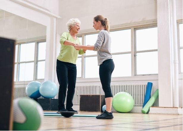 woman standing on a balance ball while a second woman holds her hand to help