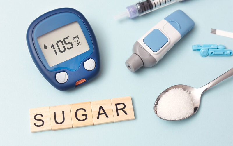 Diabetic medical supplies, a spoonful of sugar and wooden game tiles spelling "sugar" 