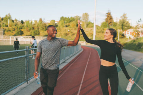 A man and woman in exercise clothing walking around a track and high-fiving