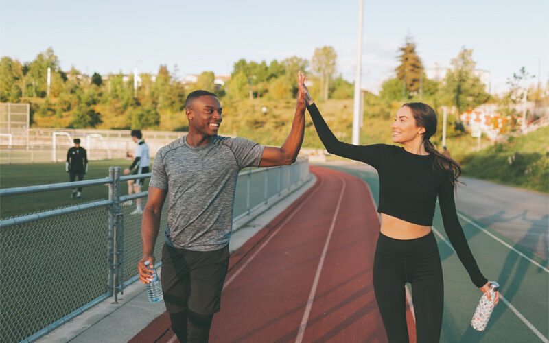 A man and woman in exercise clothing walking around a running track high-fiving each other