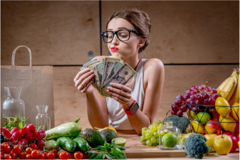 Woman looking at fan of dollar bills surrounded by fruits and vegetables