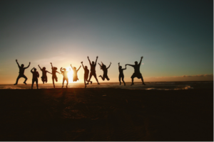 A group of people jumping and celebrating, silhouetted against a rising sun 