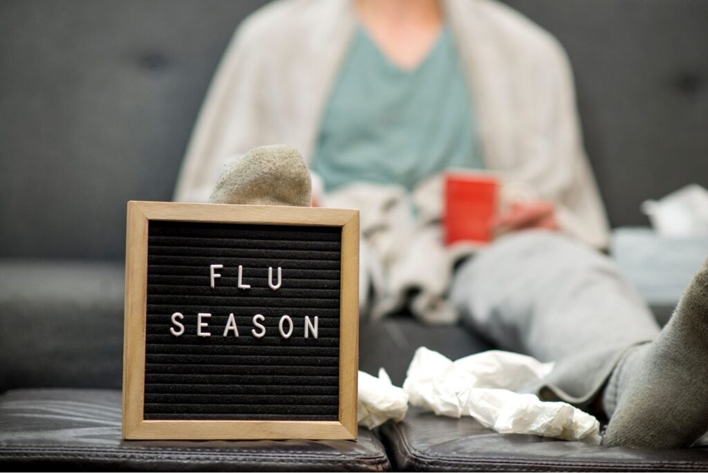 A sick person on the couch with a sign that reads "Flu Season"