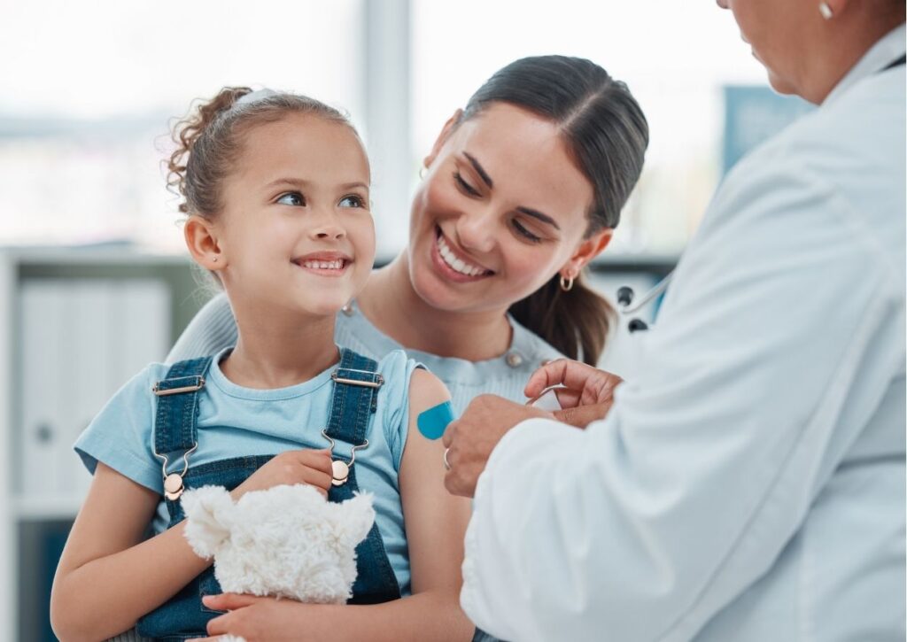 A child and mother smiling as a provider applies a bandage to the child's arm