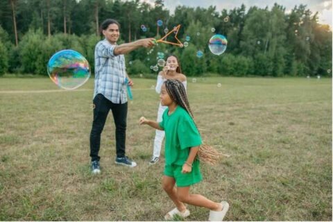 A group of three people play with bubbles in a grassy field, enjoying a sunny day in Rockledge, FL