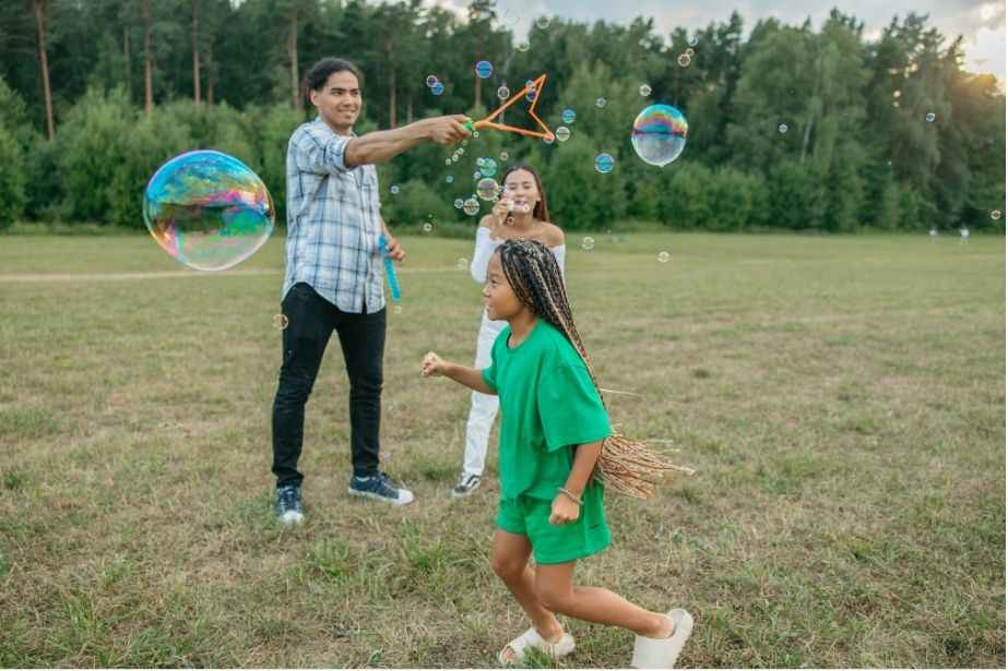 A group of three people play with bubbles in a grassy field, enjoying a sunny day in Rockledge, FL
